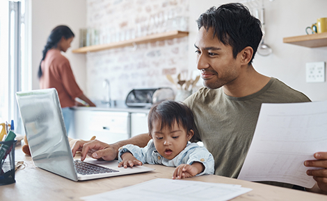 Father with child in his lap banking on his laptop.